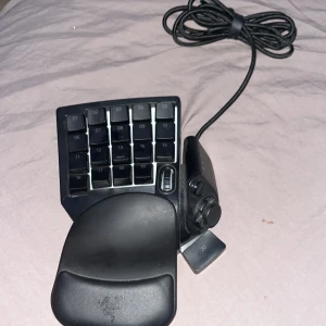 Razer Tartarus V2 - Razer Tartarus V2 gaming keypad med 20 programmerbara tangenter, tumspak och handledsstöd. Perfekt för gaming och makroanvändning. USB-anslutning, i gott skick med mindre tecken på användning. Ergonomisk design för långa spelsessioner.