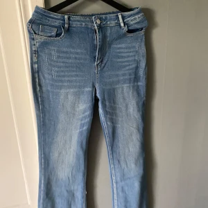 Ljusblå bootcut jeans med slitningar - Snygga ljusblå jeans med bootcut passform och diskreta slitningar framtill. Klassisk femficksmodell med dragkedja och knapp. Jeansen har en lätt tvättad look och är tillverkade i mjukt denimtyg som ger en avslappnad vibe.