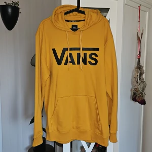Gul hoodie från Vans  - Säljer en gul hoodie från Vans i storlek Large. Tröjan har stor svart Vans-logga på bröstet, huva med snörning och en klassisk magficka.Passar dig som gillar streetwear och färg.