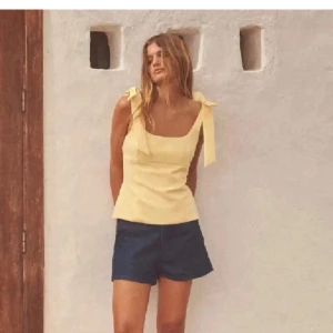 Gul topp  från Zara - Supersöt ljusgul linnetopp från Zara med breda axelband och stora rosetter på axlarna. Toppen har en figurnära passform och fyrkantig ringning som ger en trendig look. Perfekt att styla med jeans eller kjol för en fräsch sommarstil.