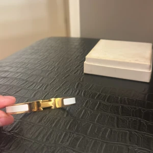 vit och guld Clic H armband - Snyggt armband Clic H armband i guldtonad metall med vita emaljdetaljer. Armbandet har den ikoniska H-formade låset och en stilren, elegant design som passar perfekt till din outfit. Kommer med original ask.