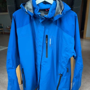 Blå Skaljacka från Didriksons - Blå Skaljacka från Didriksons med avtagbarhuva. Jackan har flera praktiska fickor. Perfekt för blöta dagar och har en sportig look.