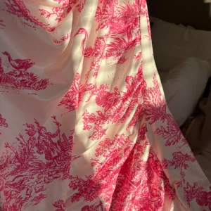 Vit och rosa långklänning från Cider - Superfin långklänning från Cider i vit med rosa mönster. Klänningen har draperad urringning och är ärmlös. Materialet är mjukt och glansigt, troligtvis polyester. Perfekt för dig som gillar romantiska vibes och snygga detaljer.