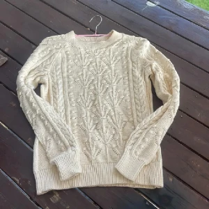 Beige stickad tröja från Part Two - Säljer en beige stickad tröja från Part Two i storlek S. Tröjan har ett snyggt flätmönster och strukturstickade detaljer framtill och på ärmarna. Mjuk och skön med ribbade muddar vid ärmslut och nederkant. Perfekt för kyliga dagar!