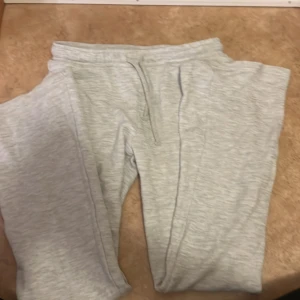 Ljusgrå mjukisbyxor från Lindex - Ljusgrå mjukisbyxor från Lindex i storlek 164. Byxorna har resår i midjan med snörning och är tillverkade i mjukt material som passar perfekt för chill dagar. Klassisk och enkel design utan tryck eller mönster.