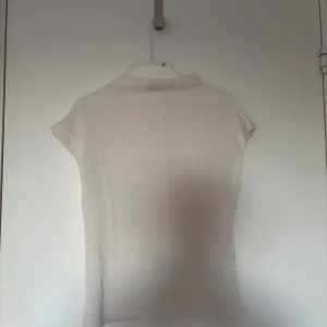 Beige ribbad topp med kort ärm - En stilren beige topp med ribbad struktur och korta ärmar. Toppen har en enkel, rak passform och liten ståkrage. Perfekt att matcha med jeans eller kjol för en clean look.