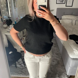 Svart stickad kortärmad topp - En svart stickad topp med korta ärmar och rund hals. Modellen är något croppad och har ribbade kanter vid ärmslut och nederkant. Perfekt för dig som gillar en enkel och stilren look med en mysig känsla.