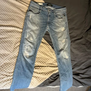 Replay Anbass ljusblå slitna jeans - Säljer ett par Replay Anbass jeans i ljusblå tvätt med slitningar och lagade detaljer på benen. Klassisk femficksmodell med normal passform och raka ben. Snyggt skinnpatch bak i midjan och diskret Replay-logga. Perfekta för en avslappnad streetstil.