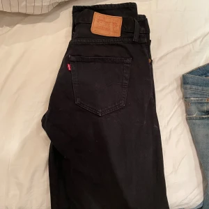 Svarta Levi's jeans straight fit - Svarta jeans från Levi's med klassisk femficksdesign och läderpatch bak i midjan. Jeansen har rak passform och är tillverkade i slitstarkt bomullstyg. Perfekta för dig som gillar en clean och tidlös look. 30/34