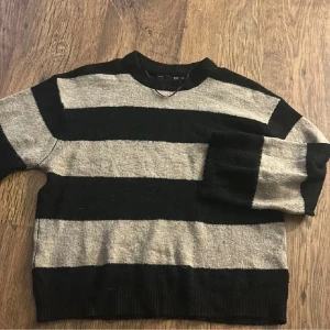 Randig svart och beige stickad tröja - Säljer en stickad tröja med breda svarta och beige ränder. Tröjan har rund halsringning och långa ärmar. Perfekt för dig som gillar en avslappnad och trendig stil. Lite knopprig annars fint skick
