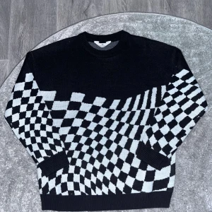 Svartvit rutig stickad tröja  - Cool stickad tröja från H&M med svart och vit rutigt mönster. Tröjan har rund hals och långa ärmar, perfekt för dig som gillar grafiska prints och vill sticka ut lite extra. Materialet är mjukt och skönt mot huden.