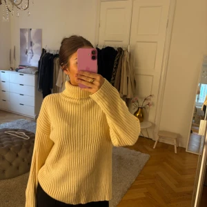 Beige/ljusgul ribbad polotröja - Säljer en beige/ljusgul ribbad polotröja med lång ärm och hög krage. Tröjan är stickad och har en loose fit med breda ärmar, perfekt för lager-på-lager. Enkel och stilren design som passar till det mesta.