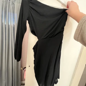 Svart oneshoulder klänning - Svart kortklänning med oneshoulder-design och lång ärm. Klänningen har en tight passform och passar perfekt i ett festligt sammanhang! Klänningen har en öppen detalj en bit under ärmen som är placerad på höften💁🏼‍♀️🙌🏼 använd två gånger!