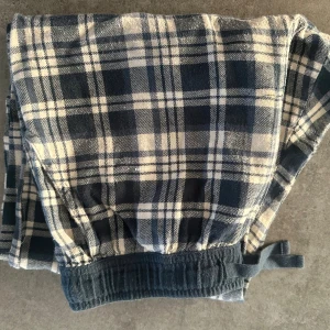 Rutiga mjukisbyxor från Kappahl - Mysiga mjukisbyxor från Kappahl i blått och vitt rutigt mönster. Byxorna har resår och snörning i midjan för extra komfort. Perfekta för chill dagar hemma eller som pyjamasbyxor.