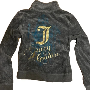 Juicy Couture grå kofta - Grå kofta från Juicy Couture med guldfärgat tryck på ryggen och snyggt broderad logga. Koftan har dragkedja framtill, två fickor och ingen luva.