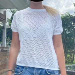 Vit blus med diamantmönster - Säljer en vit blus med korta ärmar och genombrutet diamantmönster. Toppen har rund halsringning och är tillverkad i ett lätt och luftigt material, perfekt för varma dagar. Snygg att styla med jeans eller kjol för en fräsch look.