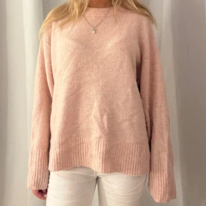 Ljusrosa stickad tröja med ribbade detaljer - Supermysig ljusrosa stickad tröja med breda ribbade muddar vid ärmslut och nederkant. Tröjan har en relaxed passform och rund halsringning, perfekt för lager-på-lager och chill dagar.