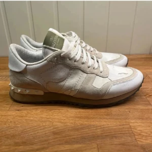 Valentino Rockrunner sneakers beige/vit - Snygga Valentino Rockrunner sneakers i beige och vitt med coola nitar på hälen. Skorna har en mix av mocka och skinn, klassisk snörning och en chunky sula med bra grepp. Perfekta för dig som vill ha en lyxig och trendig sneaker med unika detaljer.