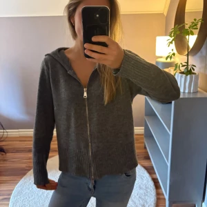 Mörkgrå stickad tröja  med dragkedja - Mysig mörkgrå stickad tröja med huva och hel dragkedja framtill. Den är tunn i materialet men skön att bära. Finns ingen lapp men är ganska säker att den är från Lindex. Storlek L men skulle säga att den är mer S