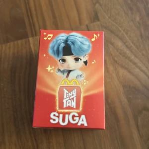 TinyTAN SUGA McDonald's Edition - Samlarfigur från TinyTAN, SUGA-version, i samarbete med McDonald's. Oöppnad originalförpackning med färgglad design och motiv av BTS-medlemmen SUGA. Perfekt för fans och samlare, inga synliga skador eller slitage på kartongen.