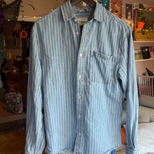 Jeansskjorta  - Säljer en ljusblå jeansskjorta från Redefined Rebel i storlek S. Skjortan har vita vertikala ränder, klassisk krage, bröstficka och knäppning framtill. Perfekt för en avslappnad och cool stil. Skjortan är snygg och ett safe val på nästa bar häng utan att riskera allt för mycket. Skjortan är snygg men sticker ut ur mängden. Fångar människors uppmärksamhet och får ofta komplimanger. Nypris 579. Använd 2 gånger, beställde fel storlek tyvärr.