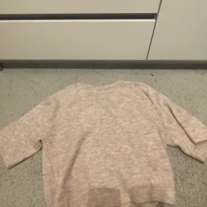 Beige stickad tröja från 157 XS - Mysig beige stickad tröja från 157 i storlek XS. Tröjan har en enkel design med rund hals och trekvartsärm. Perfekt för dig som gillar neutrala färger och vill ha en skön och avslappnad stil. Ribbstickade detaljer vid ärmslut och nederkant.