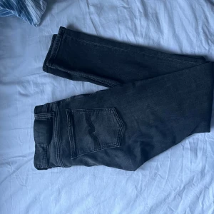 Svarta jeans från Nudie Jeans 30/32 - Säljer ett par svarta jeans från Nudie Jeans i storlek 30/32. Klassisk femficksmodell med raka ben och diskreta sömmar på bakfickorna. Jeansen är i mjuk bomullsdenim och har en mörk tvätt som passar till allt.