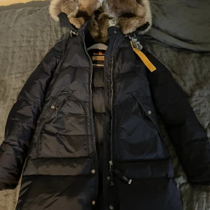 Marinblå Parajumpers dunjacka med päls - Säljer en marinblå Parajumpers dunjacka i modellen Anchorage, med fluffig päls runt huvan och snygga detaljer som stora fickor, dragkedja och patch på ärmen. Endast använd en vinter. Priset kan diskuteras vid snabb affär 