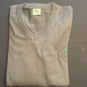 Retro Lacoste tröja  - En V-ringad retro Lacoste tröja i storlek XXL. En otroligt snygg grå och tunn tröja som man kan styla upp med massa goa grejer! Tröjan är orörd i flera år där min far var en klädsamlare. Original priset vet jag om men inte hur kostnaden idag är. Så det är förhandlingsbar!!