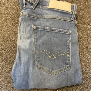 Replay ljusblå jeans, rak modell - Säljer ett par ljusblå jeans från Replay med klassisk rak passform. Jeansen har snygga kontrastsömmar på bakfickorna och ett Replay-märke i beige på linningen. Tillverkade i mjukt denimtyg som sitter skönt hela dagen.