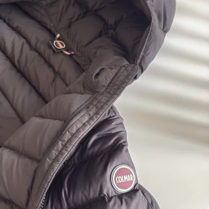 Svart Colmar pufferjacka med huva - Säljer en svart pufferjacka från Colmar med huva och två dragkedjeförsedda fickor för 1999kr. Jackan har ett stilrent, quiltat mönster och klassisk logga på ärmen. Perfekt för kalla dagar och riktigt snygg. 