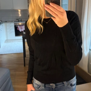 Svart stickad tröja  - En svart, klassisk stickad tröja med rund halsringning och långa ärmar. Tröjan har ribbade muddar vid ärmslut och nederkant, vilket ger en snygg och enkel look. Perfekt att matcha med jeans eller kjol.
