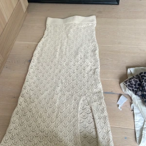 Beige långkjol i spets från H&M - Säljer en beige långkjol från H&M med snyggt spetsmönster och elastisk midja. Kjolen har en liten slits framtill och är tillverkad i ett stickat material som ger en cool och bohemisk vibe. Perfekt för dig som gillar en avslappnad men ändå trendig stil.