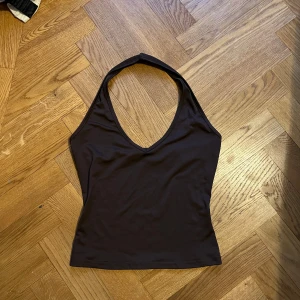 Svart halterneck linnetopp - Säljer en svart halterneck linnetopp med djup v-ringning och smal passform. Toppen är ärmlös och har en stilren, enkel design som är lätt att matcha. Materialet känns mjukt och stretchigt, perfekt för dig som gillar minimalistiska och trendiga plagg.