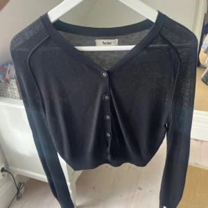 Svart tunn kofta från Acne XS - Svart, tunn och stilren kofta från Acne i storlek XS. Koftan har v-ringning, knappar framtill och långa ärmar. Materialet är lätt och känns mjukt mot huden, perfekt för lager-på-lager. Enkel att matcha med olika outfits och har en clean vibe.