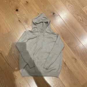 Beige hoodie med huva och snörning - En stilren beige hoodie med huva och snörning. Tröjan har lång ärm och ribbade muddar vid ärmslut och nederkant. Perfekt för en avslappnad look och enkel att matcha med andra plagg.