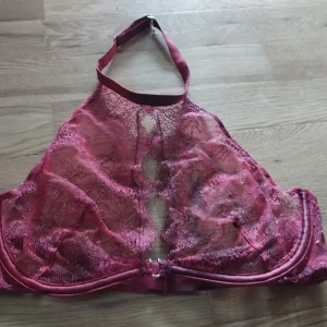 Spetsig halterneck Victoria's Secret  - Säljer en vinröd halterneck topp med transparent spets och dekorativa hål framtill. Justerbart band i nacken och spännen i ryggen. Den är färgad från klarröd till mörkare röd med variation i färgen för en kul effekt. Perfekt för dig som vill ha något unikt och vågat. Storleken passar ca 75B 