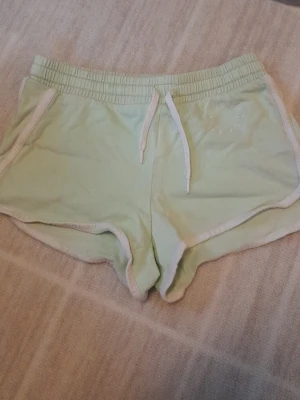 Mintgröna shorts från H&M med snörning - Säljer ett par mintgröna shorts från H&M i mjuk bomull. De har vit snörning i midjan, vita kanter och broderad text på ena sidan. Perfekta för chill dagar eller träning. Klassisk sportig look och skön passform. Stl 146. !!endast swish +frakt!!
