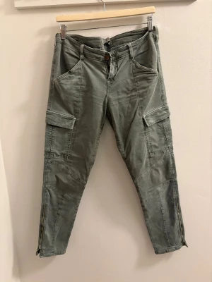 Gröna cargopants från J Brand - Snygga gröna cargopants från J Brand med flera fickor på benen och dragkedjor vid bensluten. Byxorna har en relaxed fit och är perfekta för en chill och avslappnad stil. Tillverkade i mjuk bomull för skön känsla hela dagen.