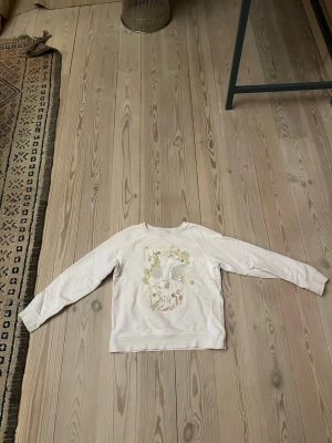 Vit sweatshirt med blommigt tryck Zadig & Voltaire 12 år  - Ljus rosa sweatshirt från Zadig & Voltaire med blommigt tryck i pastellfärger framtill. Tröjan har rund hals, långa ärmar och är gjord i mjuk bomull. Perfekt för dig som gillar en chill och stilren vibe med en twist av blommor. Storlek 12 år 152 som är xxs ungefär lite större 