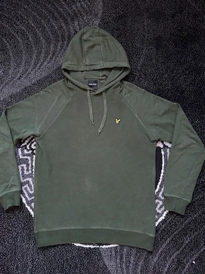 Lule& Scott OTH Fly Fleece huvtröja - Säljer en mörkgrön Lyle & Scott huvtröja i den populära Fly Fleece modellen. Tröjan är tillverkad i ett mjukt och lätt viskosbaserat fleecetyg för extra komfort.