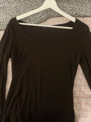 Brun  långärmad topp med bred ringning - En brun långärmad topp med bred, något asymmetrisk ringning. Tunn och mjuk i materialet, perfekt att styla med jeans eller kjol. Enkel och stilren design utan synliga detaljer.