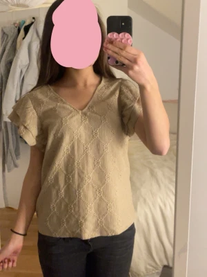Beige blus med spets från Vila - Säljer en beige blus från Vila med v-ringning och korta volangärmar. Blusen har ett broderat mönster i tyget och är tillverkad i ett lätt material som känns luftigt. Perfekt för vår och sommar, enkel att styla med jeans eller kjol. 😽😽