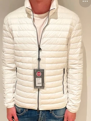 Vit pufferjacka från Colmar - Säljer en stilren vit pufferjacka från Colmar med horisontella sömmar och hög krage. Jackan har dragkedja framtill, två sidofickor med dragkedja och Colmar-logga på ärmen. Perfekt för kyliga dagar och enkel att matcha med jeans eller hoodies. Strolek 52 vilket motsvarar L. Min kille har endast använt den 2 månader men säljer den då han tycker den är för liten. Han är 186cm, så borde passa de som är runt 180-170cm långa.  