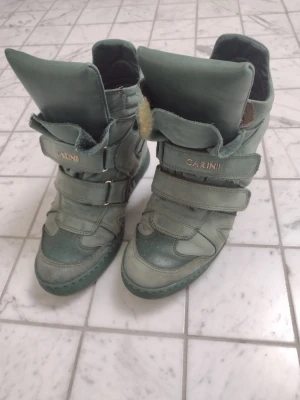 Gröna sneakers med kilklack från Carinii - Unika gröna sneakers från Carinii med kilklack och breda kardborreband. Skorna är tillverkade i mocka och har en hög plös samt rund tå. Perfekta för dig som vill ha en sportig look med lite extra höjd.