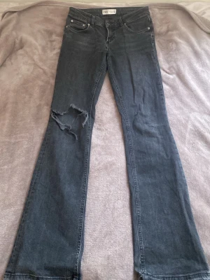 Svarta bootcut jeans från Zara - Snygga svarta jeans från Zara med bootcut-modell och slitning med hål på ena benet som jag gjort själv. Jeansen har klassisk femficksdesign, knapp och dragkedja i midjan. Materialet är jeans i bomullsmix och färgen är mörkgråsvart.