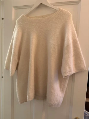 Ljusbeige oversized stickad tröja L - Supermjuk och oversized stickad tröja i ljusbeige ton. Tröjan har bred halsringning, korta ärmar och är gjord i en mix av polyester, alpacka och ull. Perfekt för lager på lager och chill höst- och vinterdagar.