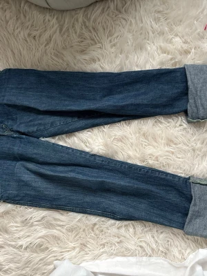 Blå jeans med breda uppvik - Säljer ett par klassiska blå jeans med breda uppvik nertill. Jeansen har raka ben och bakfickor med kontrastsömmar. Perfekta för en avslappnad och trendig look. Materialet är slitstarkt jeans och färgen är mörkblå.