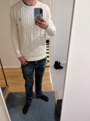 Vit kabelstickad tröja Polo Ralph Lauren - Säljer en klassisk vit kabelstickad tröja från Polo Ralph Lauren. Tröjan har rund hals, ribbade muddar och den ikoniska lilla loggan på bröstet. Perfekt för jeans. Tröjan har inga slitningar. Sitter tight runt armarna, fråga gärna vid minsta frågetecken. Öppen för bud! 