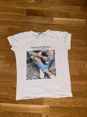 Vit t-shirt med tryck från Angelo Blu - Snygg vit t-shirt från Angelo Blu i storlek XL med ett coolt street style-tryck framtill och texten 'MODA DI STRADA street culture'. Klassisk passform och rund hals. Perfekt för dig som gillar trendiga och avslappnade looks.